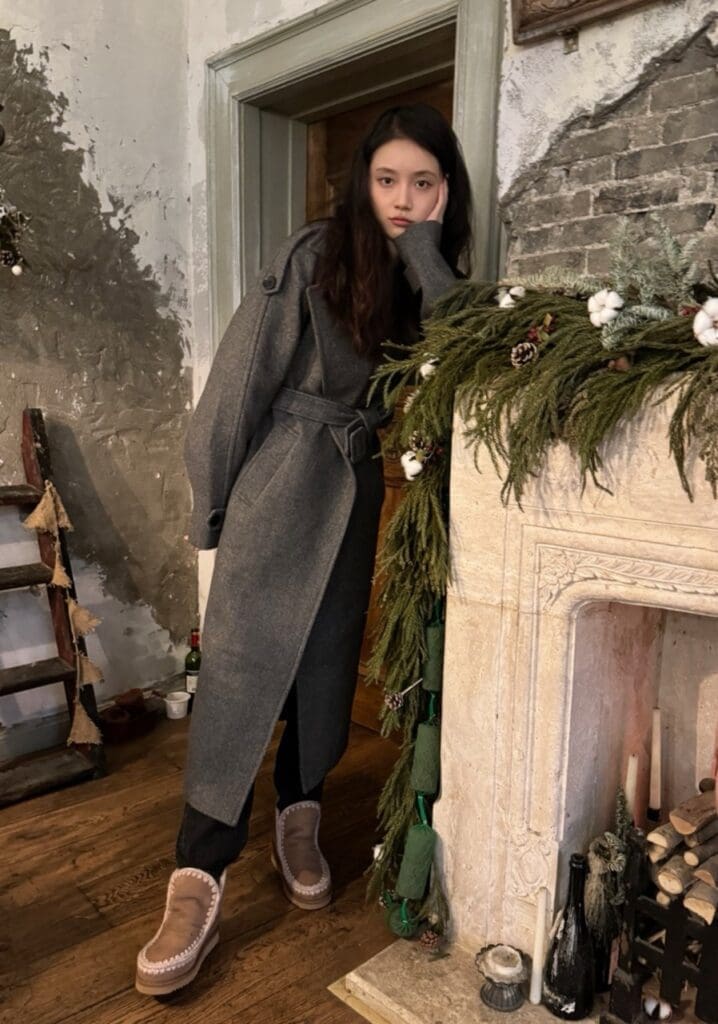 Chinese celebrity in a Christmas-decorated room leaning on fireplace wearing mou shoes